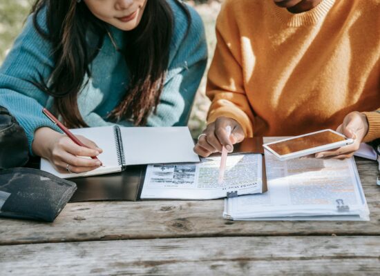 crop diverse female students fulfilling homework together in park